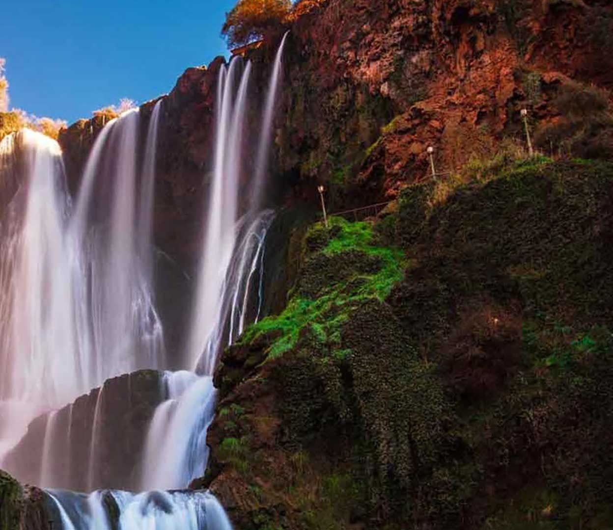 The main Ouzoud falls in warm evening light, streams dropping between green rock