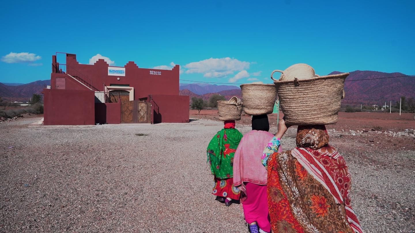 Women carrying woven baskets on a village road in the Ouzoud region